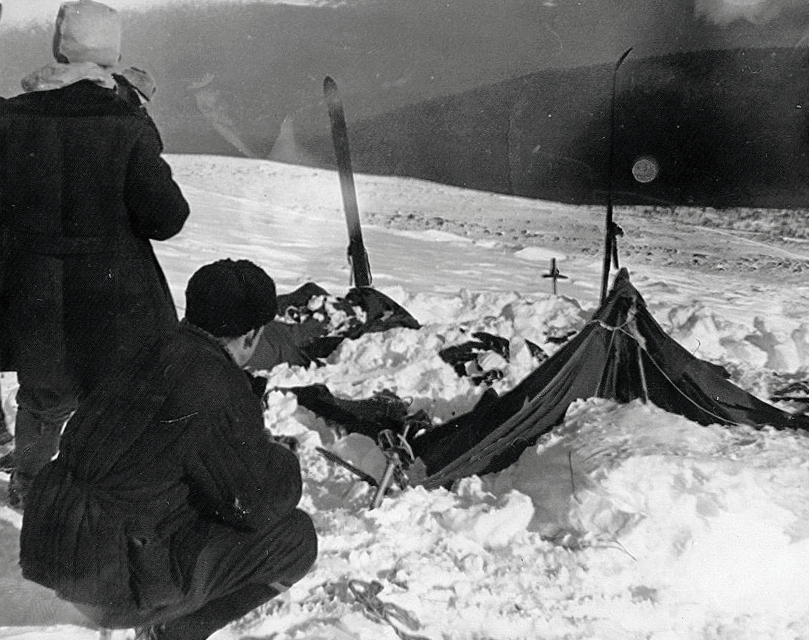 Two men look at a broken tent surrounded by snow.